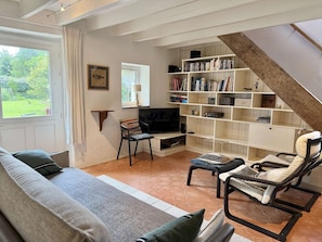 Ein Wohnzimmer mit einer Couch, einem Fernseher, einem Bücherregal und einer Treppe.