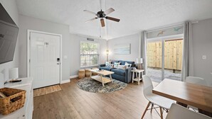 A modern living room with a ceiling fan, a sofa, a coffee table, and a dining area. - Checkmate Cottage - Fire Pit + Putting Green (Palm Harbor)