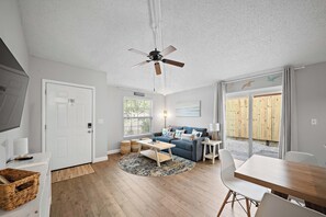 A modern living room with a ceiling fan, a sofa, a coffee table, and a dining area. - Checkmate Cottage - Fire Pit + Putting Green (Palm Harbor)