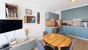 A compact kitchen with blue cabinets, a wooden dining table, and a flat-screen TV. - QUIBERON - 2 rooms - 33m2 - City center (QUIBERON)