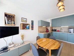 A compact kitchen with blue cabinets, a wooden dining table, and a flat-screen TV. - QUIBERON - 2 rooms - 33m2 - City center (QUIBERON)