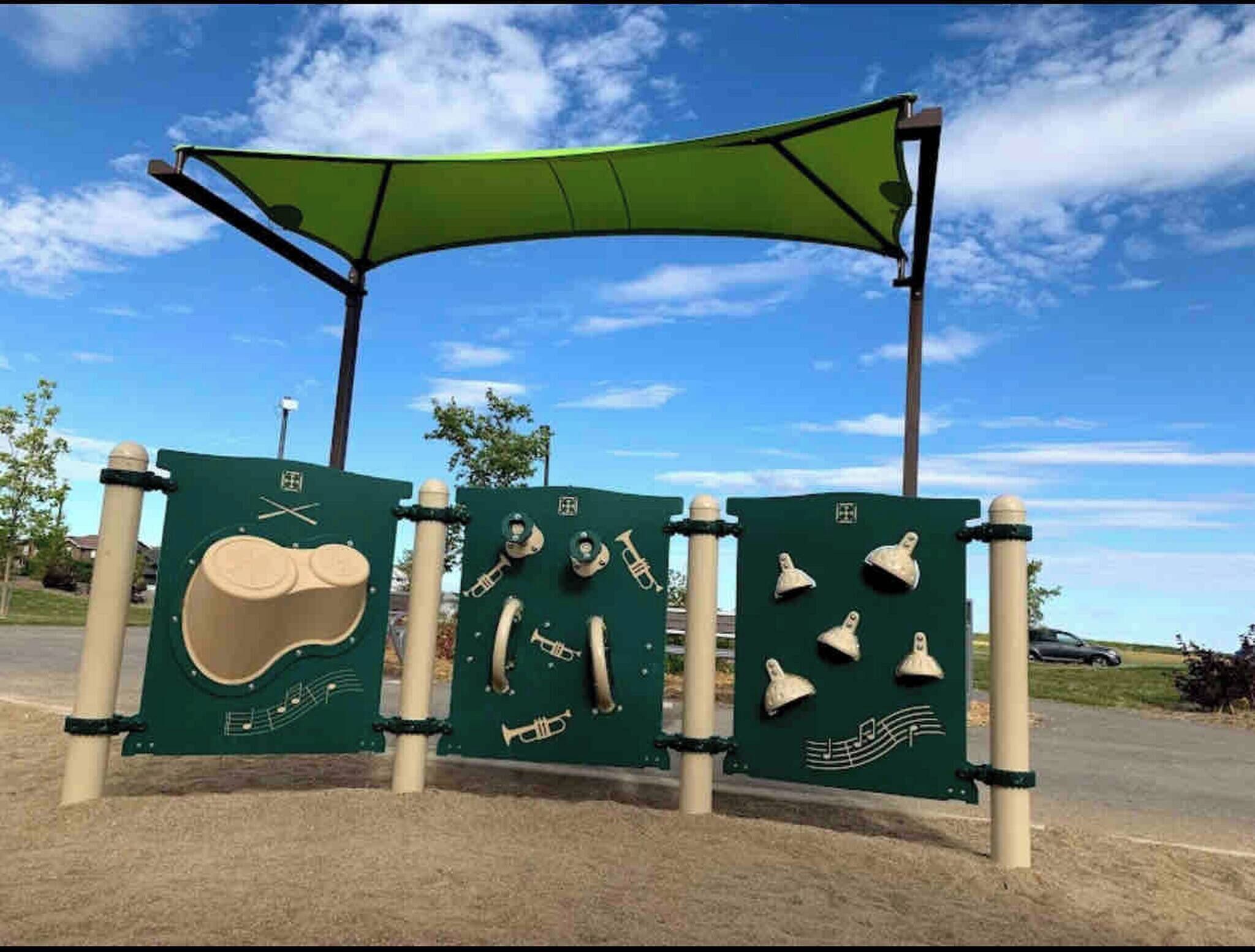 Un parque infantil con instrumentos musicales y un toldo verde.