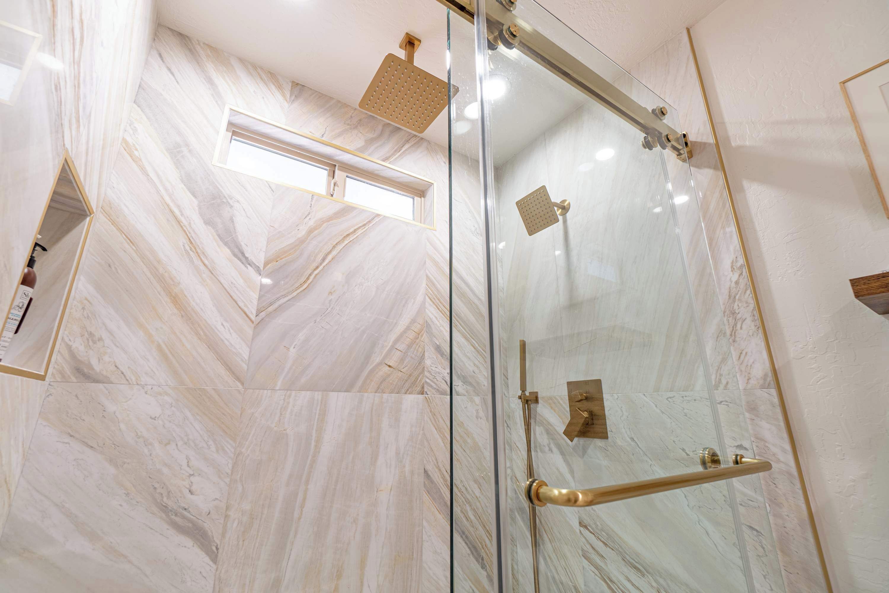 Un bagno moderno con cabina doccia in vetro, pareti in marmo e soffione dorato.