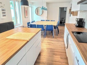 Een moderne keuken met een houten aanrecht, een eetgedeelte met blauwe stoelen, en uitzicht op de omgeving.