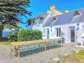 Un bâtiment situé sur la côte, avec un banc en bois, un chemin de gravier et un ciel bleu dégagé.