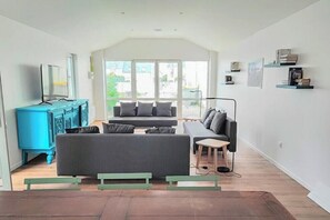 Un salon moderne avec un canapé, une table basse et un téléviseur. On y trouve également des étagères et une fenêtre donnant sur un beau paysage.