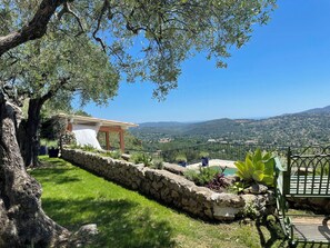 A stone retaining wall, a grassy area, a stone building with a tiled roof, and a view of distant hills. - Apartment with panoramic views near Cannes (Spéracèdes)