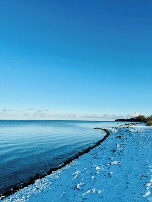 Ein schneebedeckter Strand mit blauem Himmel und ruhiger See.