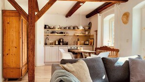 Een gezellige woonkamer met een balken plafond, een bank met kussens, een eettafel en een keuken met kasten en apparatuur.