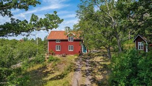 Une maison rouge avec un toit en pente, entourée d’arbres et bordée d’un chemin de terre.