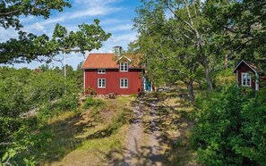 Ett rött hus med ett sluttande tak, omgivet av träd och en grusväg.