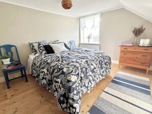 Un dormitorio con cama, cómoda, una silla con planta y una ventana.