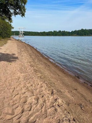 En sandstrand med ett badvakts torn och en lugn sjö.