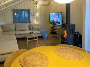 En hyggelig stue med sofa, fjernsyn, et lille bord og en pejs.
