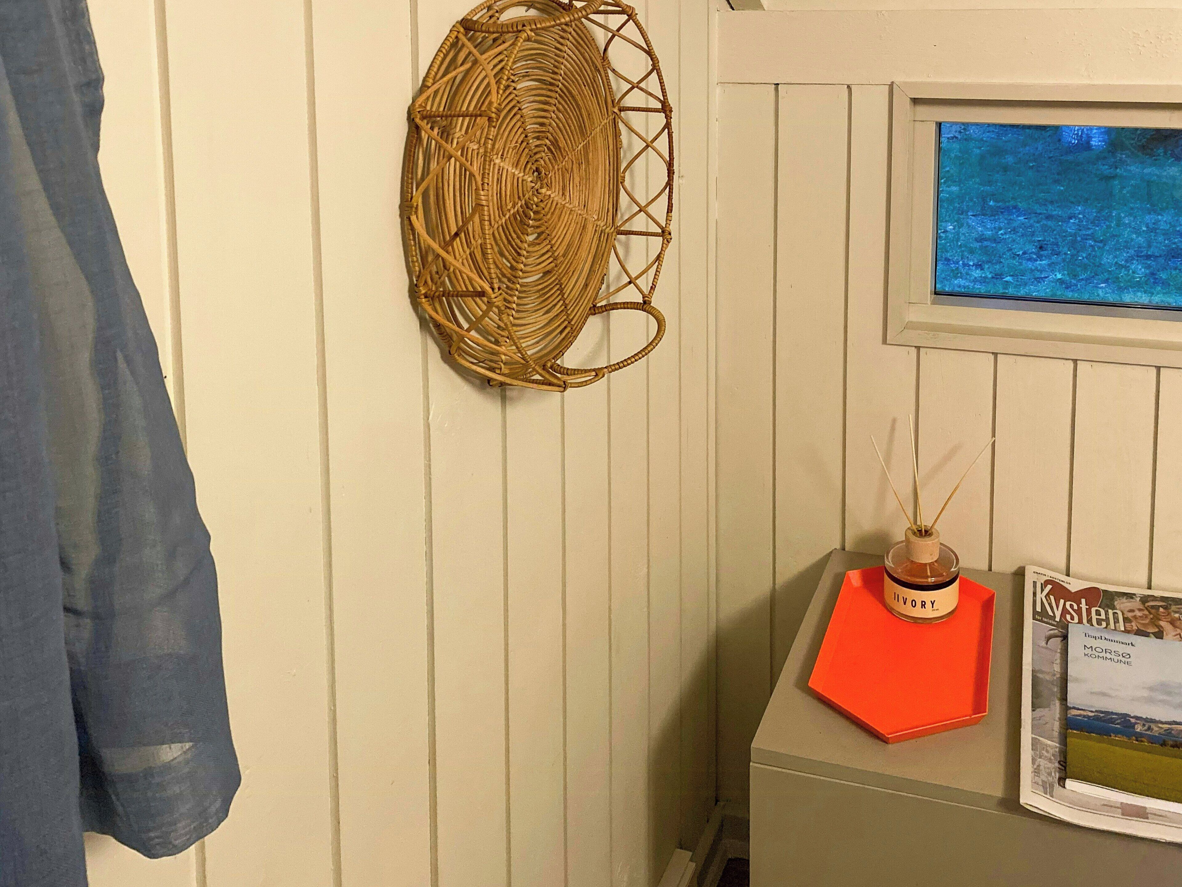 A room with a woven wall hanging, a framed picture, and a small table with a bottle and a card.