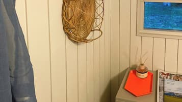 A room with a woven wall hanging, a framed picture, and a small table with a bottle and a card.