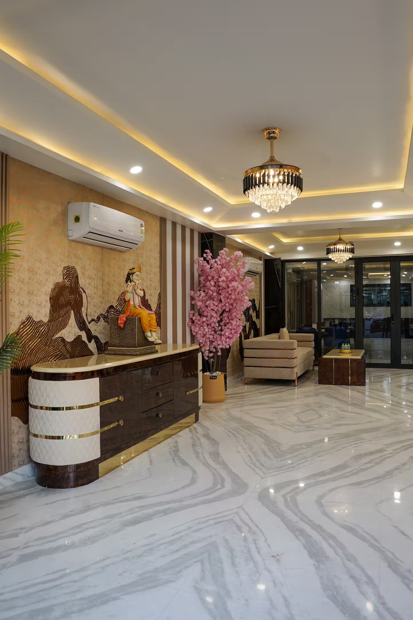 A modern reception area with a marble floor, a reception desk, a chandelier, and a large pink floral arrangement.