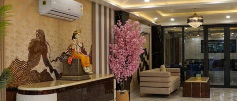 A modern reception area with a marble floor, a reception desk, a chandelier, and a large pink floral arrangement.