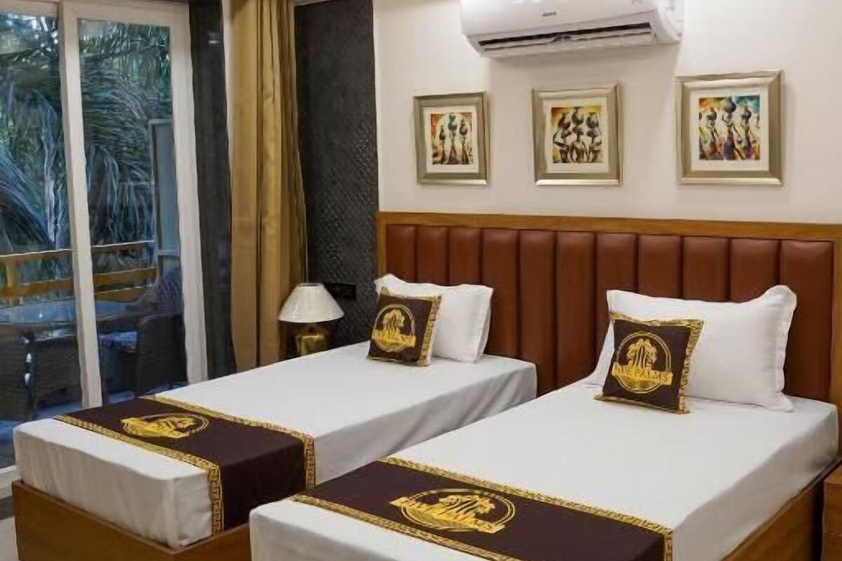 A hotel room with two beds, a ceiling fan, an air conditioning unit, and a window with a view.
