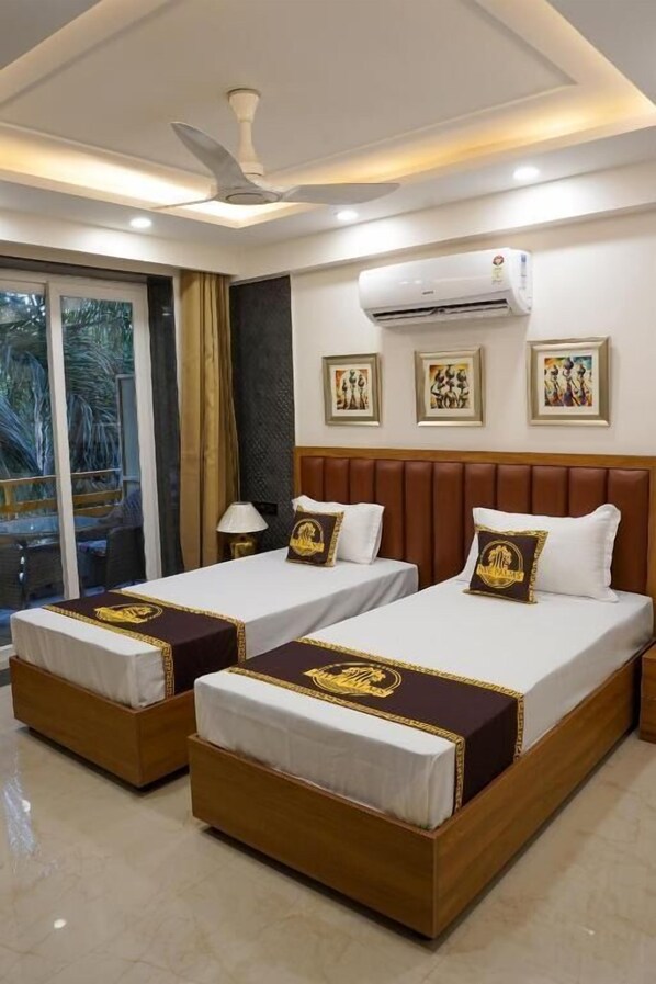 A hotel room with two beds, a ceiling fan, an air conditioning unit, and a window with a view. - Five Palms Hotels (Gurugram)