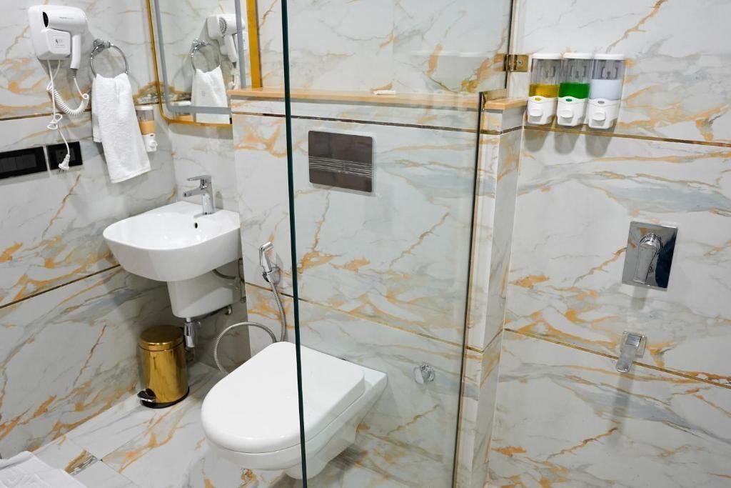 A bathroom with a glass-enclosed shower, a sink, a toilet, and a hairdryer on the wall.