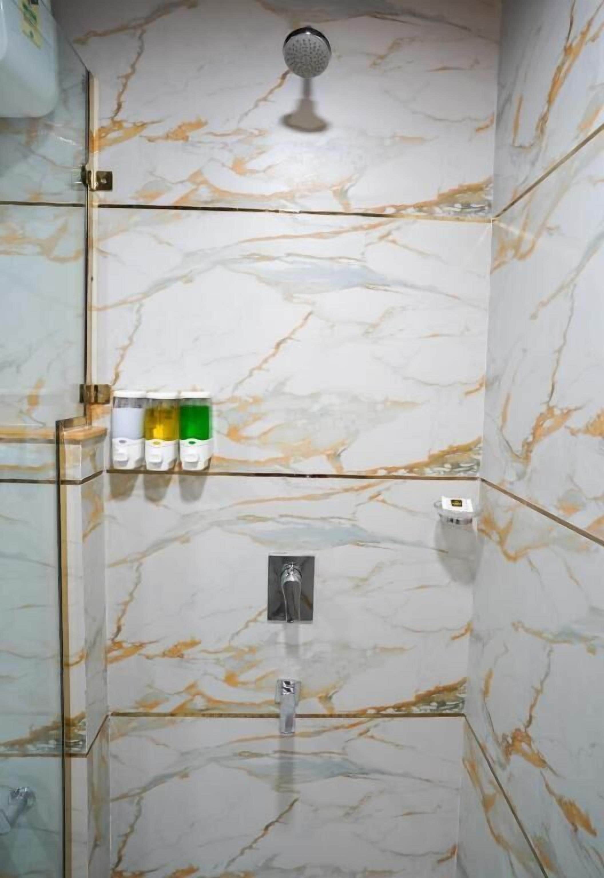 Un baño con ducha, paredes de mármol y un estante con artículos de aseo.