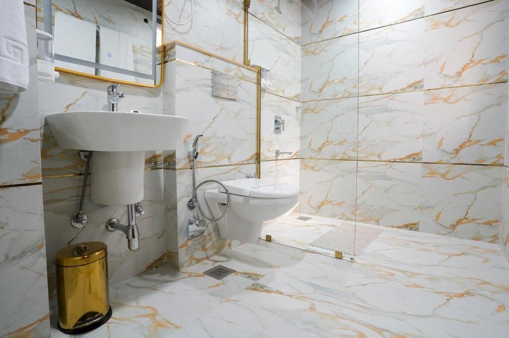 A bathroom with a sink, toilet, and shower area, featuring marble walls and gold fixtures.