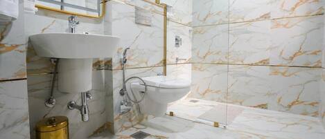 A bathroom with a sink, toilet, and shower area, featuring marble walls and gold fixtures.