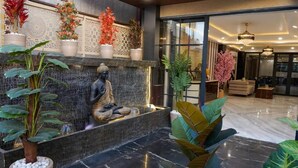 A modern lobby with a stone fountain, indoor plants, and a Buddha statue.