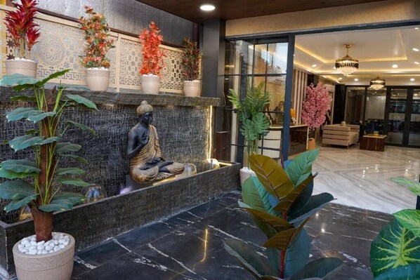 Um lobby moderno com uma fonte de pedra, plantas e uma estátua de Buda.