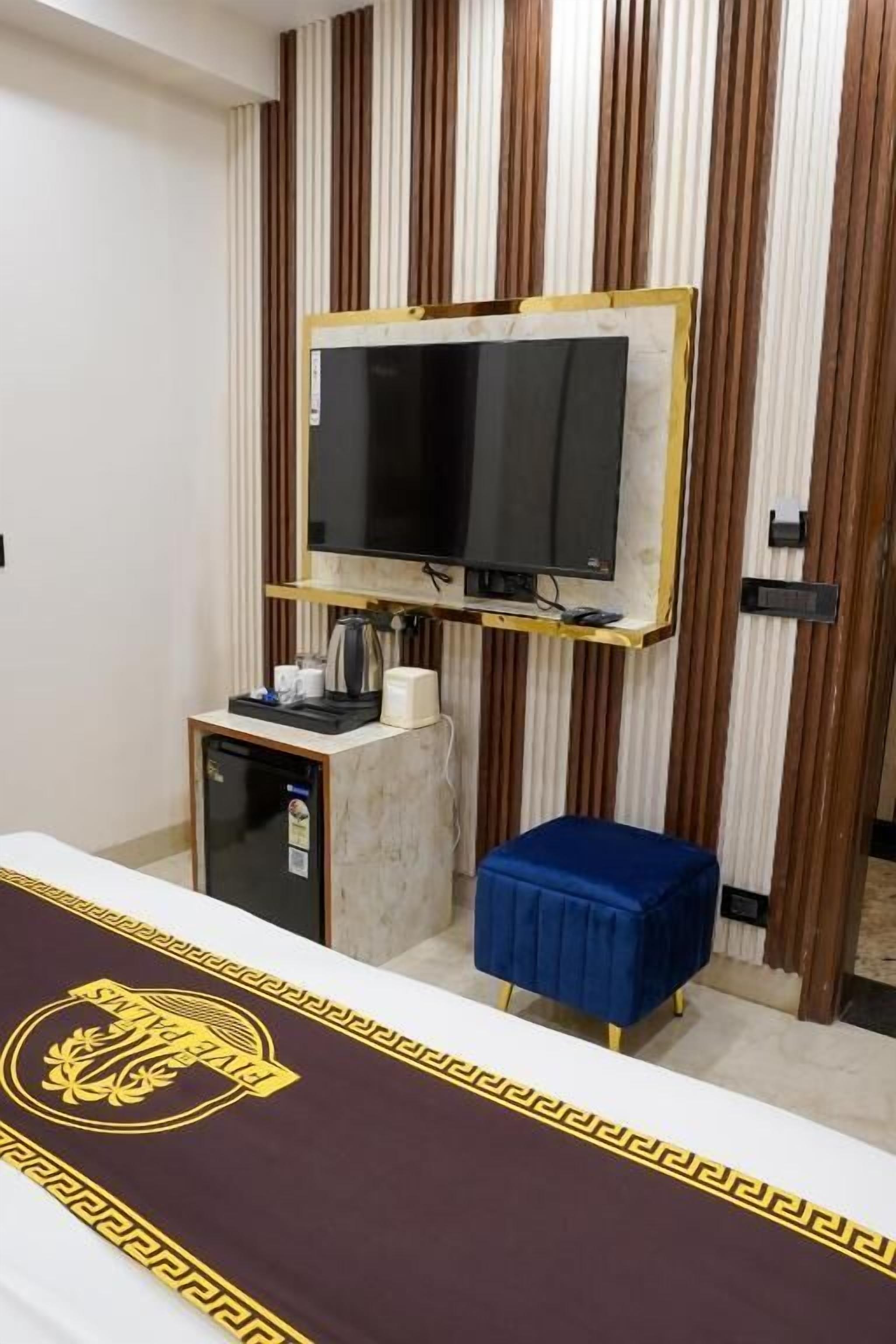 Habitación de hotel con cama, televisor montado en la pared, una mesita con cafetera y un reposapi és azul.