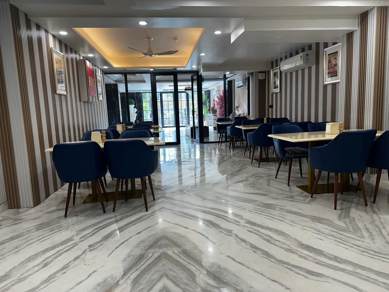 A hotel lobby with a marble floor, blue chairs, and a ceiling fan.