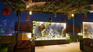 A rooftop bar with a green wall, ceiling fans, and a seating area with cushions. - Five Palms Hotels (Gurugram)