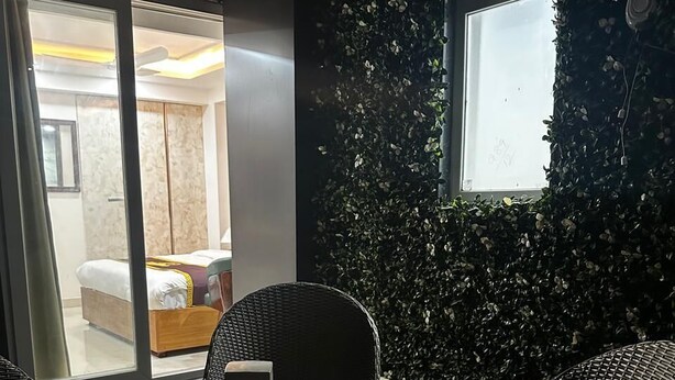 A room with a round table, wicker chairs, a bed with a colorful blanket, and a window with a view of another room. - Five Palms Hotels (Gurugram)