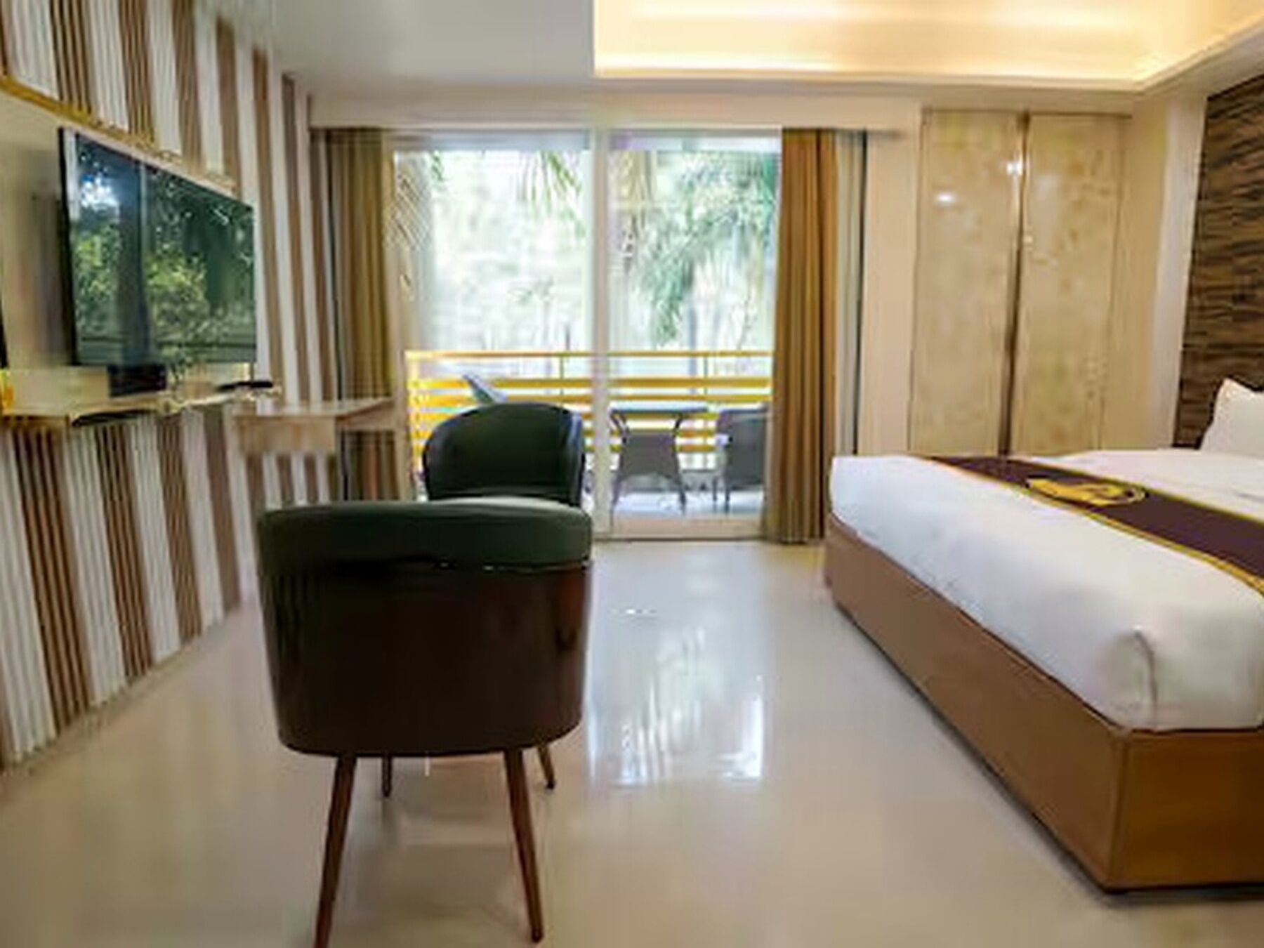 A hotel room with a bed, a TV mounted on the wall, a chair, and a balcony with a view of palm trees.