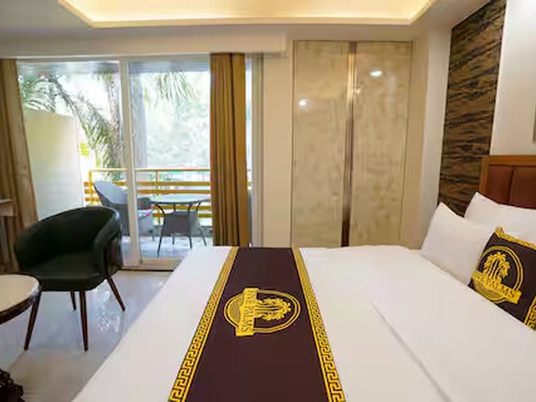 A hotel room with a bed, a chair, a table, and a balcony with curtains.