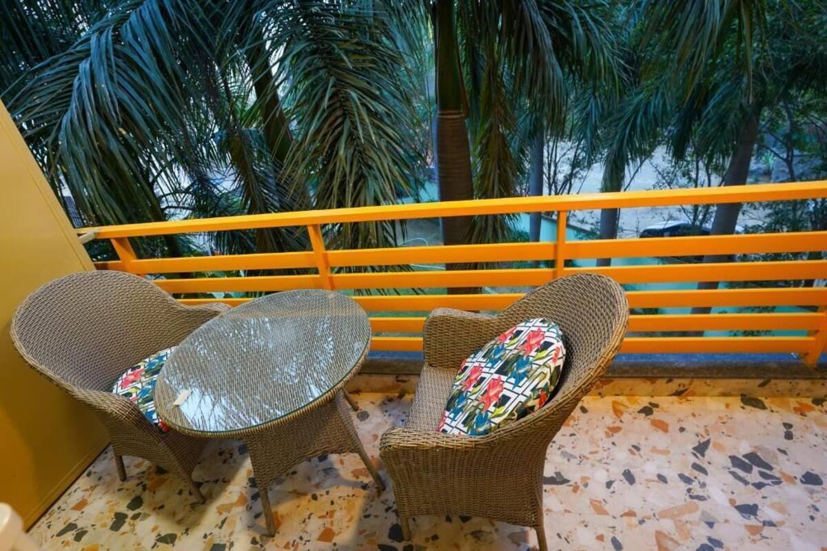 A balcony with wicker furniture, a glass table, and a view of palm trees.