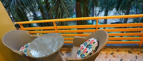 Uma varanda com móveis de vime, uma mesa de vidro e vista para palmeiras.