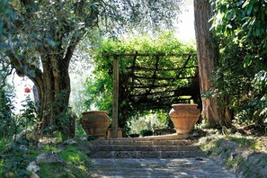 Ein Kiesweg führt zu einer Holzpergola mit Terrakottatöpfen.