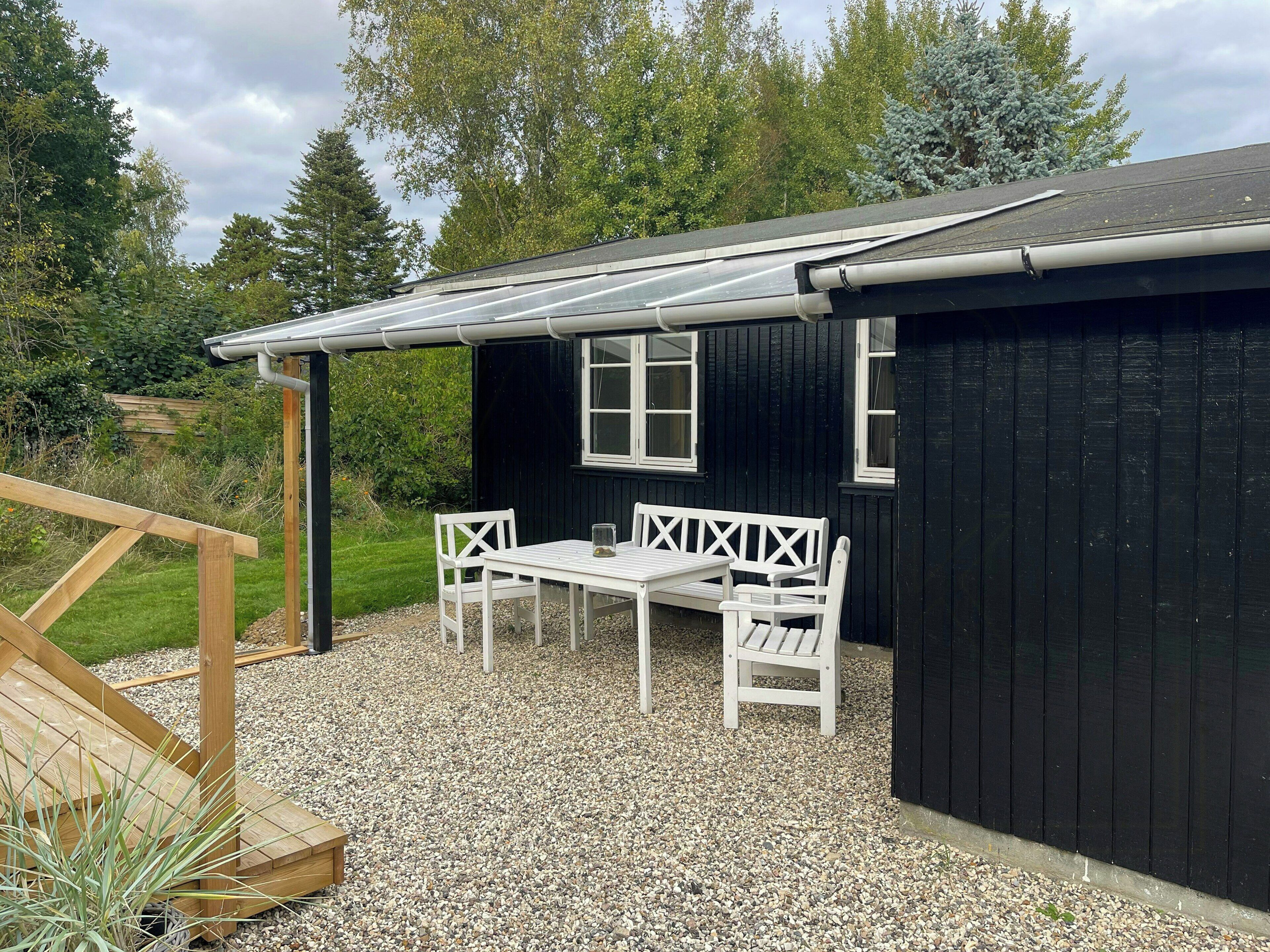A black building with a white table and chairs, gravel ground, and a wooden deck.