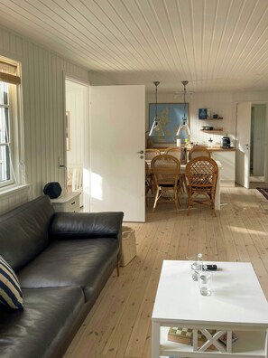 A modern living room with a leather sofa, a white coffee table, and a dining area with wicker chairs and a map on the wall. - Summer house with sauna near Udsholt Beach (Græsted)