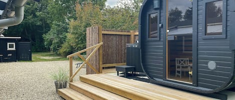 A compact, modern cabin with a wooden deck, a small outdoor seating area, and a large window.