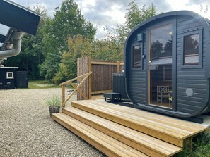 Una cabana compacta i moderna amb un terraço de fusta, una petita zona d'estar a l'exterior i una finestra gran.