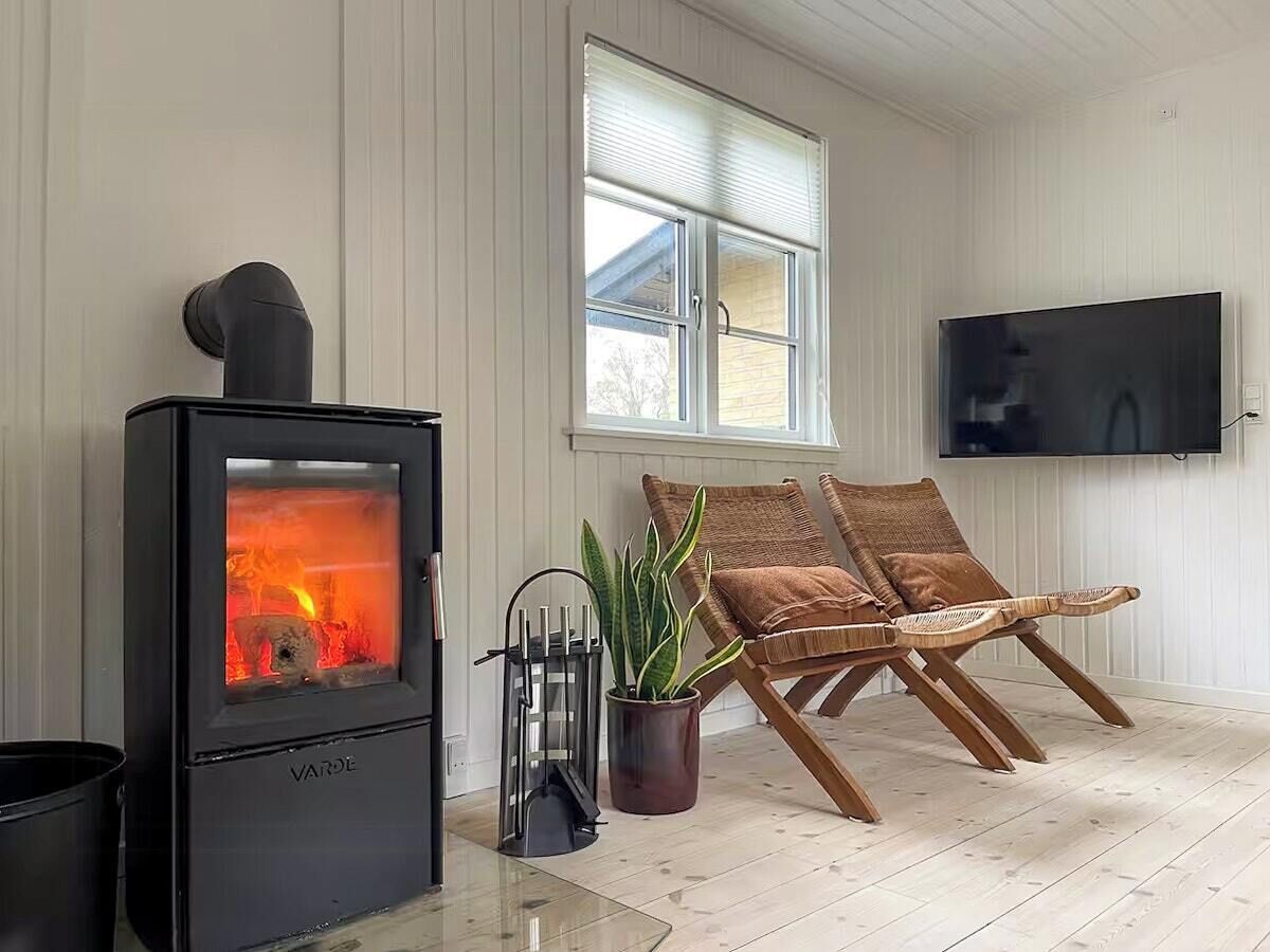 A room with a wood-burning stove, a TV mounted on the wall, and two wicker chairs.