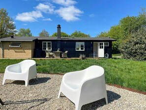 A house with a patio, two white chairs, a table, and a small garden area. - Summer house with sauna near Udsholt Beach (Græsted)