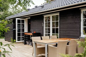 A wooden cabin with a deck, a table, and chairs. - Home among trees with architectural flair (Dronningmølle)