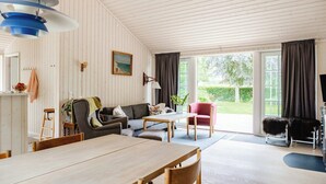 Ein geräumiges Zimmer mit Esstisch, einer Sofagarnitur, einem Sessel und einem großen Fenster mit Vorhängen.
