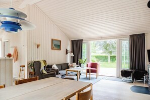 A spacious room with a dining table, a sofa set, a chair, and a large window with curtains. - Home among trees with architectural flair (Dronningmølle)