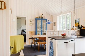 A kitchen with a blue cabinet, a dining table with chairs, a sink, and a window. - Home among trees with architectural flair (Dronningmølle)