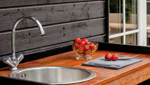 Eine Küche mit einer Holzwand, einem Edelstahlspülbecken und einer Schüssel Erdbeeren auf der Arbeitsfläche.